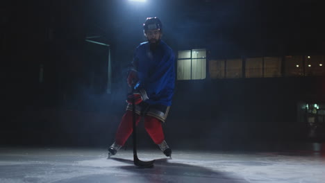Ein-Männlicher-Eishockeyspieler-Mit-Einem-Puck-Auf-Der-Eisbahn-Zeigt,-Wie-Er-Sich-Beim-Dribbeln-Direkt-In-Die-Kamera-Bewegt-Und-Vor-Einem-Dunklen-Hintergrund-Im-Rauch-Direkt-In-Die-Kamera-Blickt